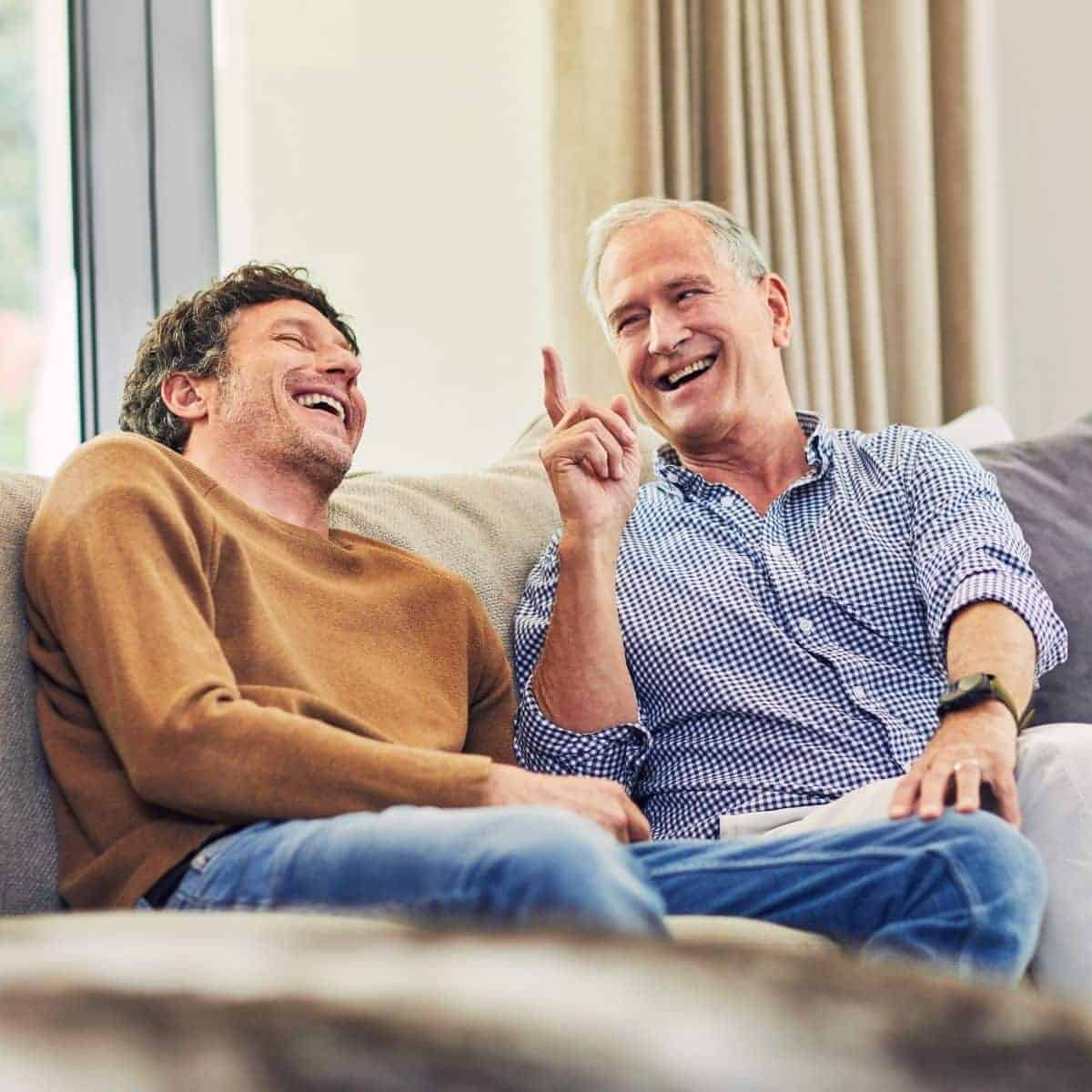 Two men sitting on a couch and laughing.