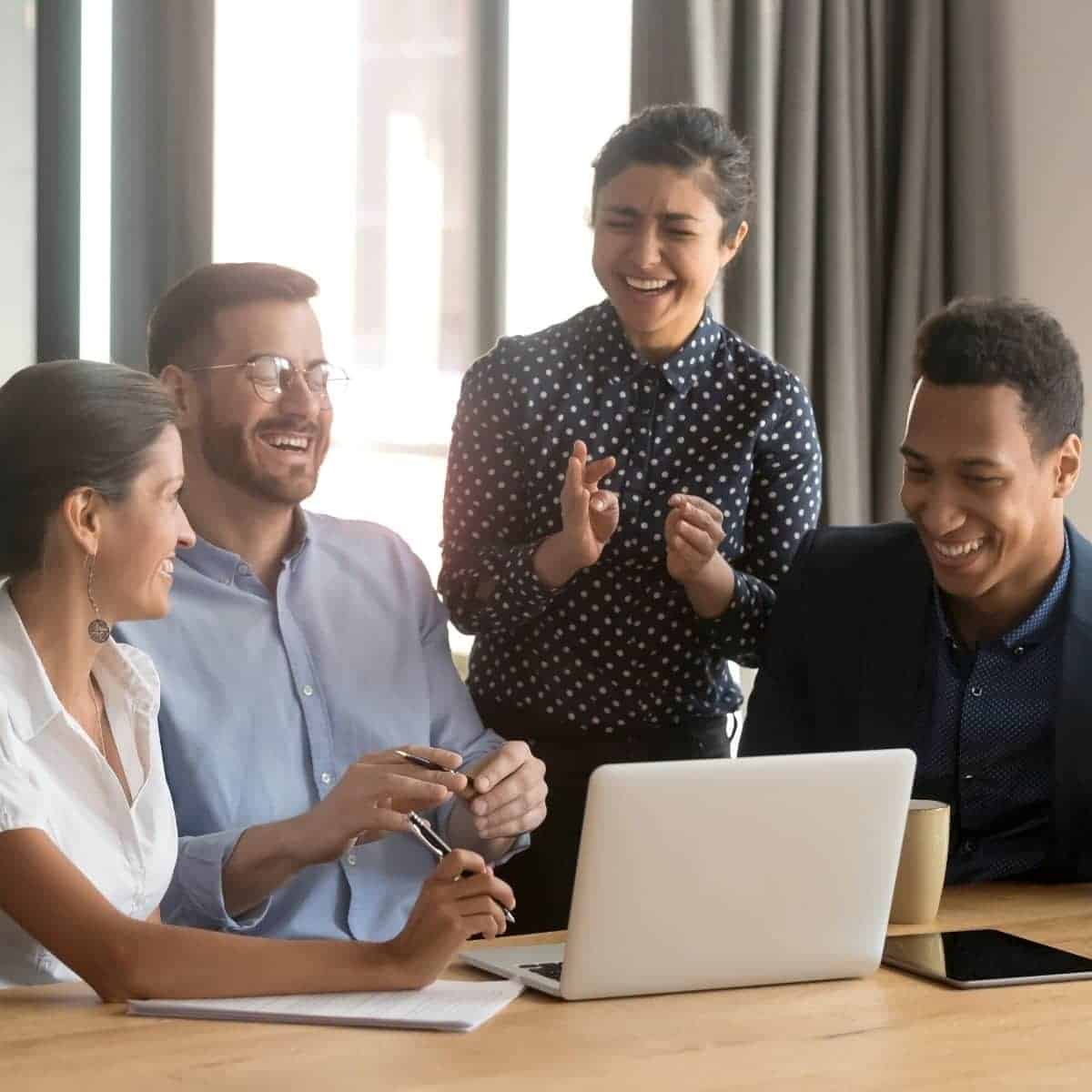 People at laughing at a table and looking at a laptop.